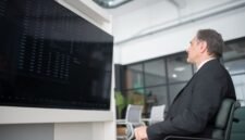 Gambar menunjukkan seorang profesional yang sedang menganalisis data di depan layar komputer yang menampilkan berbagai grafik, melambangkan kompleksitas dan pentingnya strategi bisnis digital berbasis data. Ini menggambarkan bagaimana perusahaan modern memanfaatkan teknologi untuk memahami tren pasar dan perilaku konsumen.