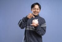 Seorang wirausahawan muda sedang serius menghitung dan merencanakan alokasi dana, menunjukkan pentingnya manajemen keuangan yang cermat sebagai modal awal membangun sebuah usaha. Meja di depannya dipenuhi catatan dan perangkat yang mendukung perencanaan strategis untuk mencapai tujuan bisnis.