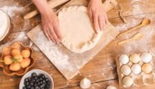 Seorang wanita sedang bekerja di meja dapur yang tertata rapi, dikelilingi oleh peralatan memasak dan bahan kerajinan, menggambarkan suasana produktif di rumah. Gambar ini merepresentasikan berbagai potensi usaha yang dapat dikembangkan dari rumah sendiri.