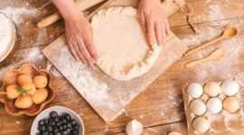 Seorang wanita sedang bekerja di meja dapur yang tertata rapi, dikelilingi oleh peralatan memasak dan bahan kerajinan, menggambarkan suasana produktif di rumah. Gambar ini merepresentasikan berbagai potensi usaha yang dapat dikembangkan dari rumah sendiri.