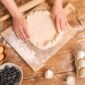 Seorang wanita sedang bekerja di meja dapur yang tertata rapi, dikelilingi oleh peralatan memasak dan bahan kerajinan, menggambarkan suasana produktif di rumah. Gambar ini merepresentasikan berbagai potensi usaha yang dapat dikembangkan dari rumah sendiri.
