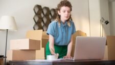 Seorang wanita tengah fokus bekerja di meja kerjanya yang tertata rapi di rumah, dikelilingi oleh berbagai peralatan seperti laptop, buku, dan beberapa dekorasi tanaman yang menunjukkan suasana kantor rumahan yang nyaman dan produktif. Ia sedang menjalankan salah satu ide usaha rumahan kreatif yang memungkinkannya mengelola bisnis dari kenyamanan rumah sendiri.