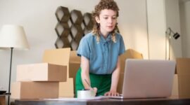 Seorang wanita tengah fokus bekerja di meja kerjanya yang tertata rapi di rumah, dikelilingi oleh berbagai peralatan seperti laptop, buku, dan beberapa dekorasi tanaman yang menunjukkan suasana kantor rumahan yang nyaman dan produktif. Ia sedang menjalankan salah satu ide usaha rumahan kreatif yang memungkinkannya mengelola bisnis dari kenyamanan rumah sendiri.