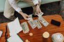 Seorang wanita tengah menghitung tumpukan koin yang dikumpulkan dalam toples, melambangkan upaya menabung secara konsisten untuk modal awal sebuah usaha. Gambar ini merefleksikan semangat wirausaha dalam mengelola keuangan pribadi.