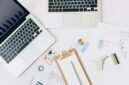 Seorang pebisnis wanita profesional tampak menganalisis data grafik pada layar tabletnya, menggambarkan proses pengambilan keputusan berbasis data yang krusial dalam strategi bisnis digital. Di latar belakang, terlihat elemen visual yang merepresentasikan konektivitas global dan pertumbuhan digital.